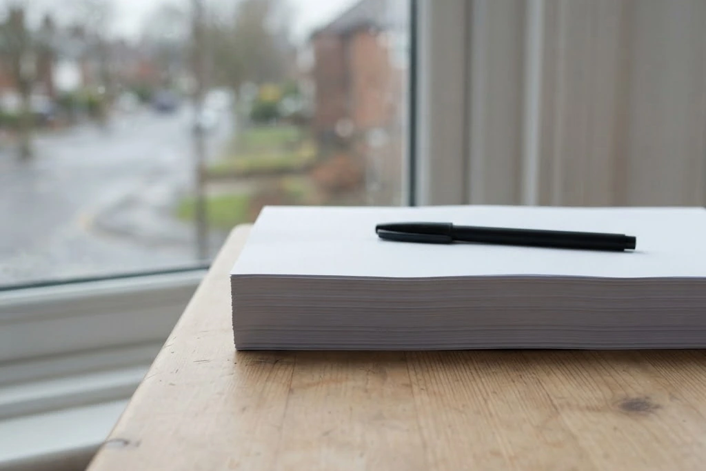 A stack of plain paper and a pen on a desk beside a window, for owner reporting in Brampton
